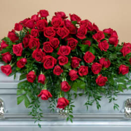 Red rose casket spray with trailing greenery on a silver casket