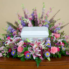 Casket spray with pink and purple flowers and white lilies