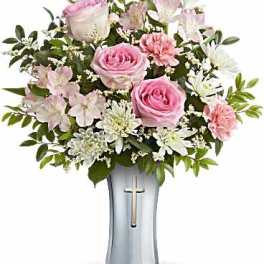 Pink roses and white flowers arranged in a silver vase with a cross