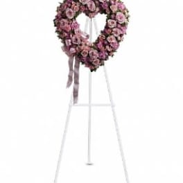 Heart-shaped pink floral wreath on a white stand with ribbon