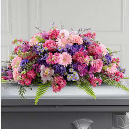 Pink and purple casket spray with gerbera daisies, roses, and carnations on a gray casket