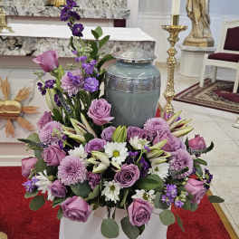 Lavender and white floral arrangement around a gray urn in a church