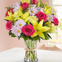 Bouquet of pink roses, yellow lilies, and pale daisies in a glass vase