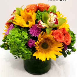 Colorful arrangement of sunflowers, orange roses, green hydrangeas, and orchids in a cylinder vase