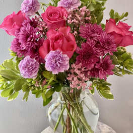 Bouquet of peach and pink roses with purple carnations in a glass vase