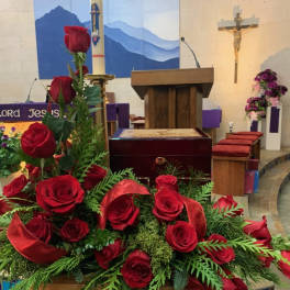Red roses arranged in a church setting with red ribbon accents