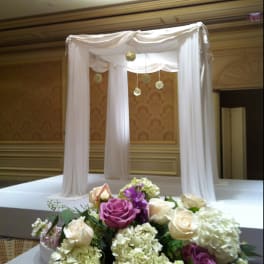 Purple and cream rose arrangement in front of a white draped canopy