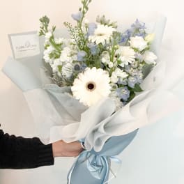 Bouquet of white gerbera daisies and pale blue flowers wrapped in white paper