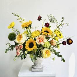 Mixed bouquet with sunflowers, roses, and yellow blooms in a gray pedestal vase