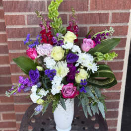 Mixed bouquet of roses, chrysanthemums, and purple flowers in a white vase