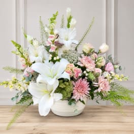 White lilies and pink mixed flowers arranged in a white bowl vase
