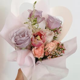 Handheld bouquet of pastel roses and tulips wrapped in pale pink paper