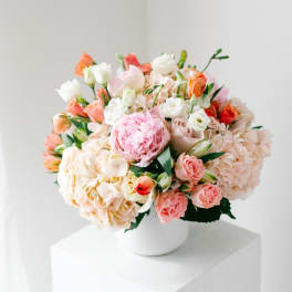 Mixed bouquet of pink, peach, and white flowers in a white vase