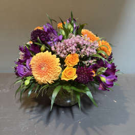 Mixed bouquet of orange, purple, and pink flowers in a glass vase