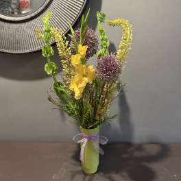 Yellow flowers and purple allium in a green vase with a ribbon