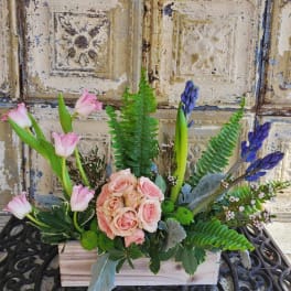 Pink roses and tulips arranged in a wooden box with purple blooms