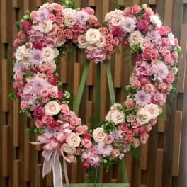 Heart-shaped floral wreath of pink and white roses with a ribbon bow