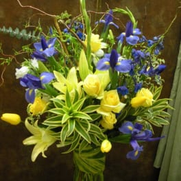 Blue irises and yellow roses in a tall glass vase