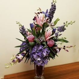 Purple and pink floral arrangement in a tall glass vase