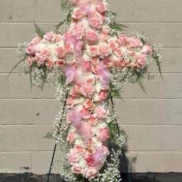 Pink floral cross on a stand with ribbon and white filler flowers