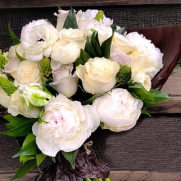 White rose and peony bouquet with green accents wrapped in dark paper