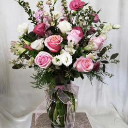 Pink and white rose bouquet in a glass vase with a pink ribbon