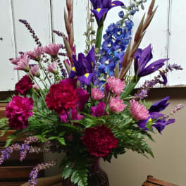 Tall mixed bouquet of purple, pink, and blue flowers in a dark glass vase