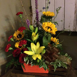 Mixed bouquet with sunflowers, lilies, roses, and carnations in a red container