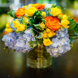 Bouquet of orange and yellow roses with blue hydrangeas in a glass vase