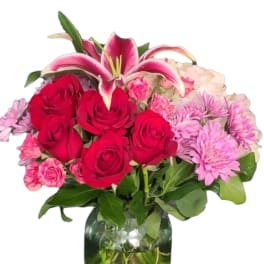Bouquet of red roses, pink lilies, and lavender daisies in a glass vase