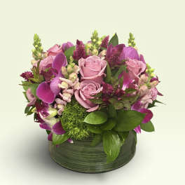 Pink roses and purple orchids arranged in a low green vase