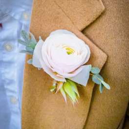 White boutonniere with small blue-green foliage pinned to a tan jacket