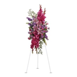 Tall standing floral spray with pink lilies and purple flowers on a white easel