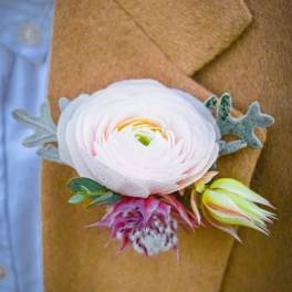 White ranunculus boutonniere with pink and yellow accents on a tan jacket