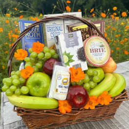 Wicker gift basket filled with fruit, cheeses, snacks, and orange flowers.