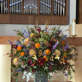Large mixed floral arrangement in a tall vase with orange, purple, red, and white blooms