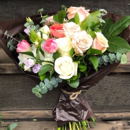 Bouquet of pastel roses and tulips wrapped in dark paper