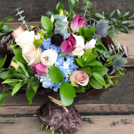 Mixed bouquet of roses, tulips, and blue flowers wrapped in dark paper