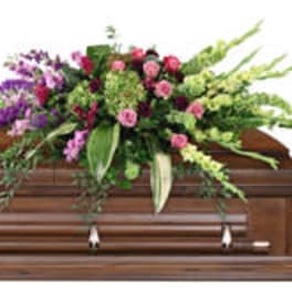 Floral spray on a wooden casket with pink, purple, and green blooms