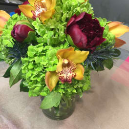 Bouquet of green hydrangeas with yellow orchids and burgundy peonies in a glass vase