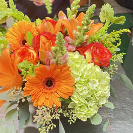 Bright orange and red mixed bouquet with green hydrangea in a black container