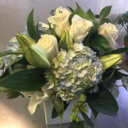 White roses and pale blue hydrangeas in a square vase