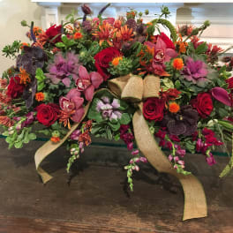 Large floral arrangement with red roses, orchids, and orange blooms tied with burlap ribbon