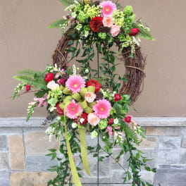 Floral wreath with pink gerberas, roses, and greenery on a grapevine frame