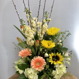 Mixed floral arrangement with sunflowers, gerbera daisies, tulips, and pale blooms in a wooden box