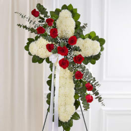 Standing floral cross with white blooms and red roses on an easel