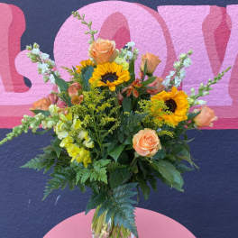 Mixed bouquet with sunflowers, peach roses, and yellow snapdragons in a glass vase