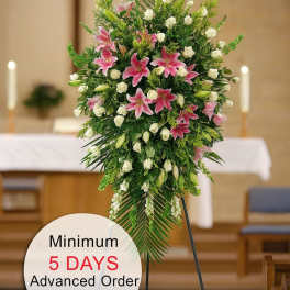 Tall standing spray with pink lilies and white roses on a metal easel in a church.