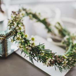 Floral crown with small white blossoms and green sprigs beside a glass lantern