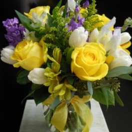 Yellow roses and white tulips in a glass vase with purple accents
